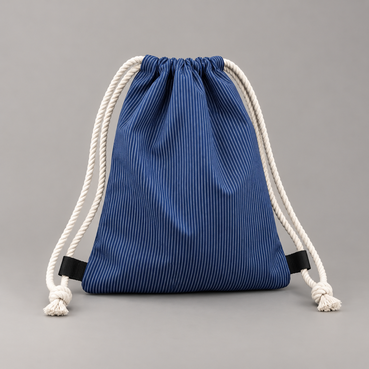 Pfälzer Rucksack aus blauem Winzerstoff mit feinen weißen Streifen und Baumwollkordeln auf grauem Hintergrund.